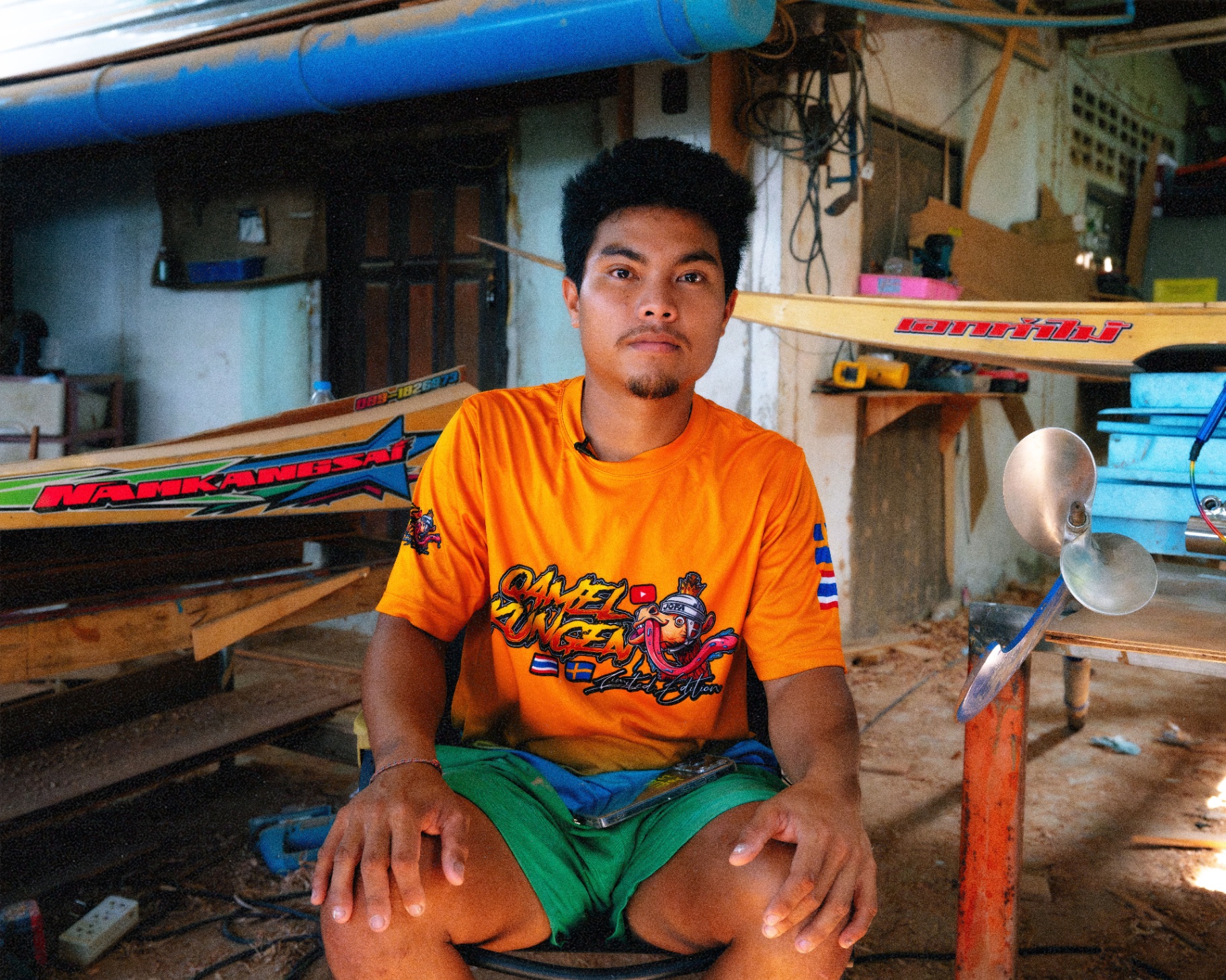 A young racer sits in front of his boats and propellers in the workshop