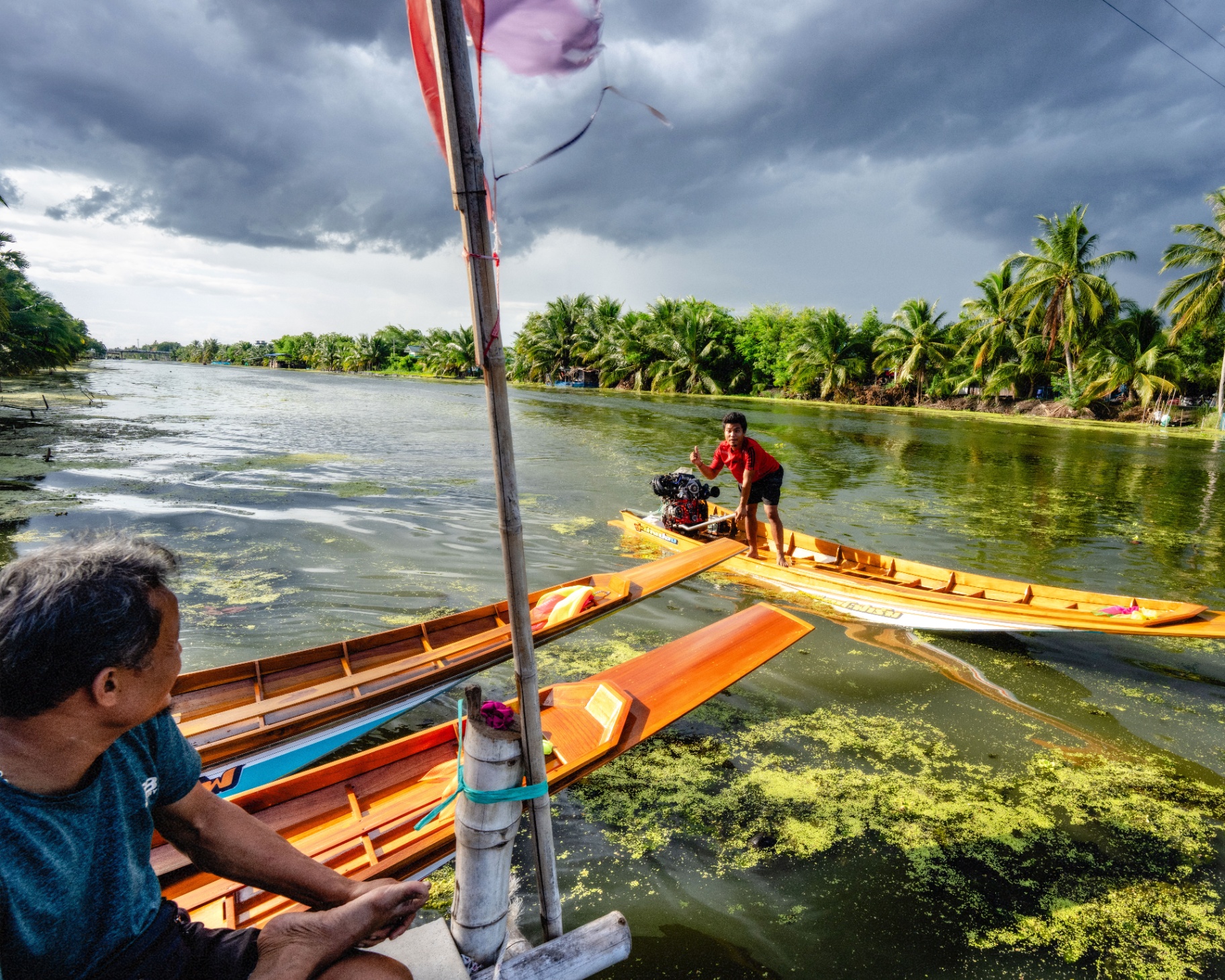 Two longtail racing boats on a green river under stormy skies