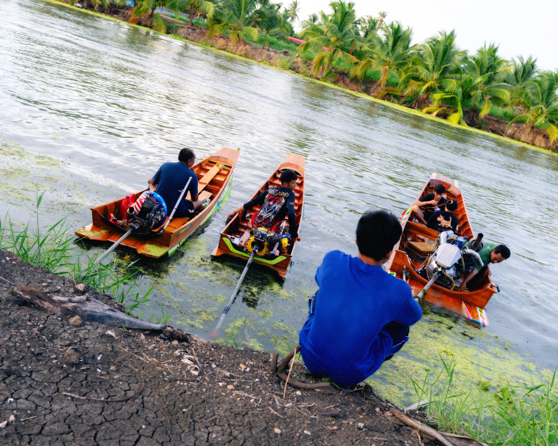 Three longtail boats lined up along the muddy bank