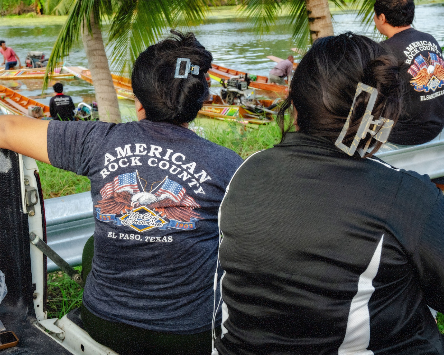 Two women in American Rock County shirts watch the boats from the bank